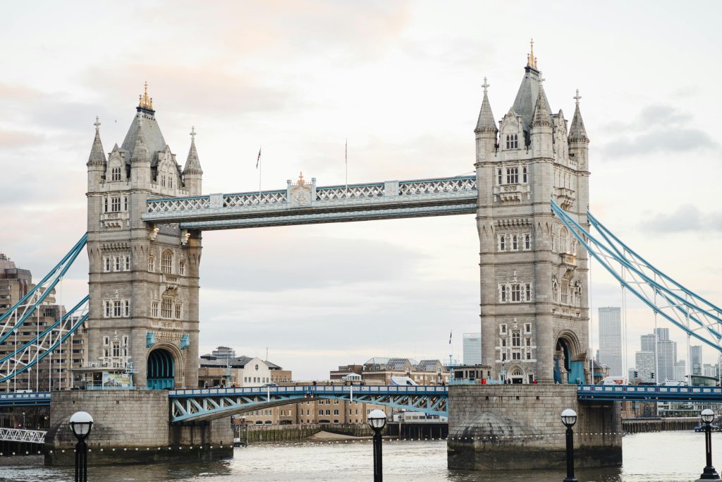 pexels-photo-7245327-7245327 Historic suspension bridge with towers connected by walkways located over calm river against residential buildings in London city against cloudy sky